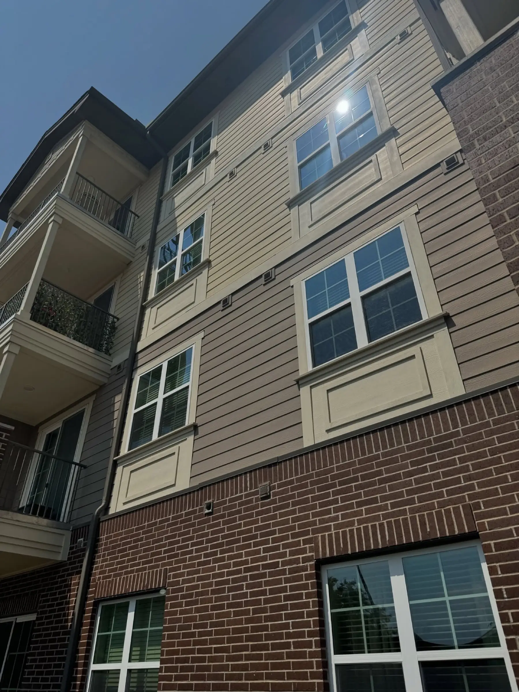 Upper floors of a four-story senior living building in brick and painted siding, windows clean and reflecting open sky