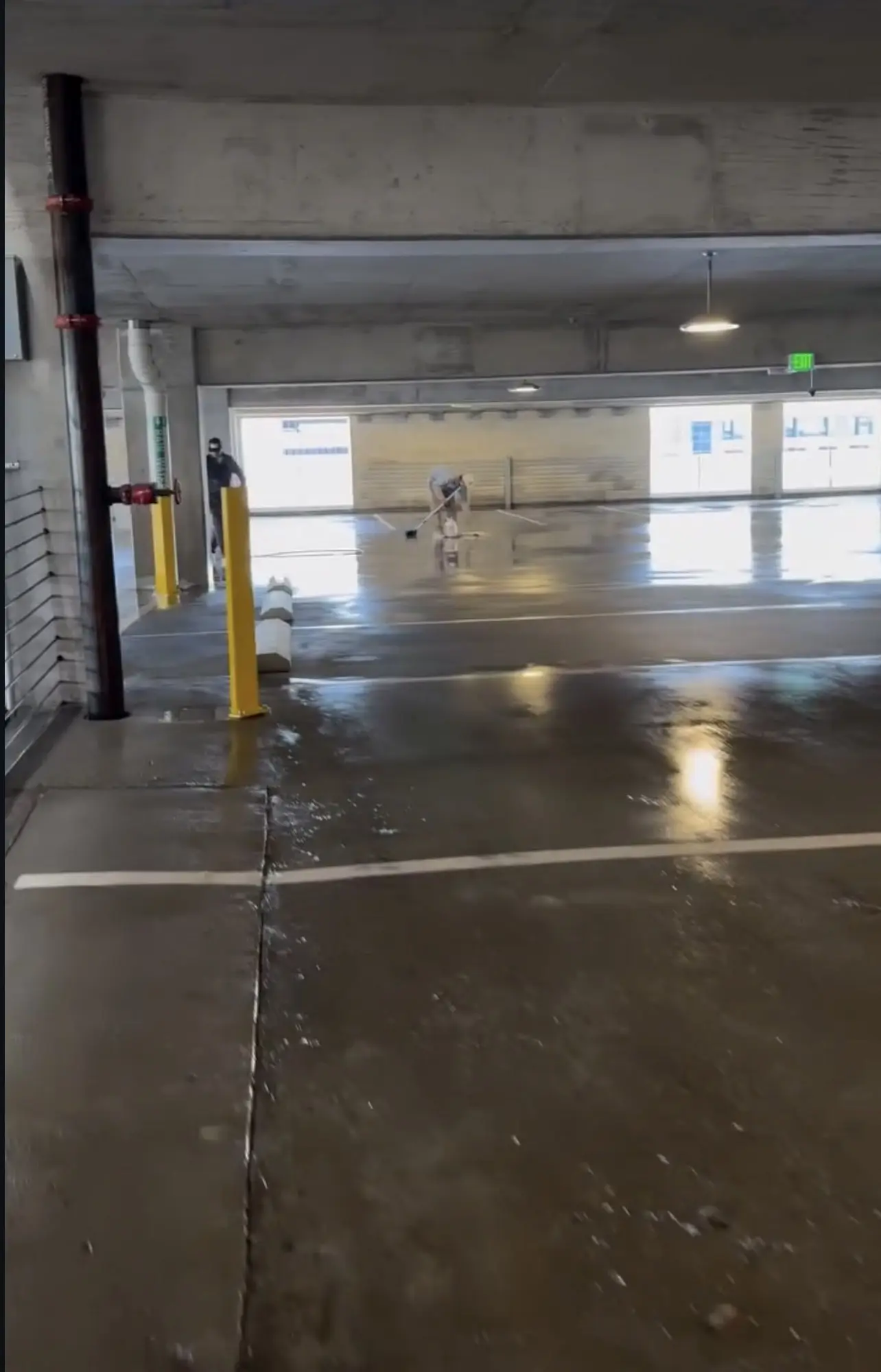 A finished parking deck level, the concrete washed down and even, daylight coming through the openings along the far wall and two crew members working at the end of the bay