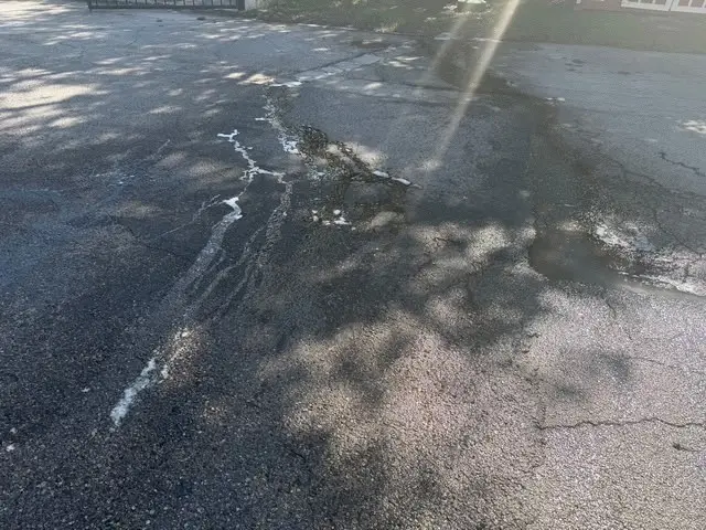White degreaser foaming along the cracks in the asphalt behind the restaurant, dark grease staining spread across the surface around it