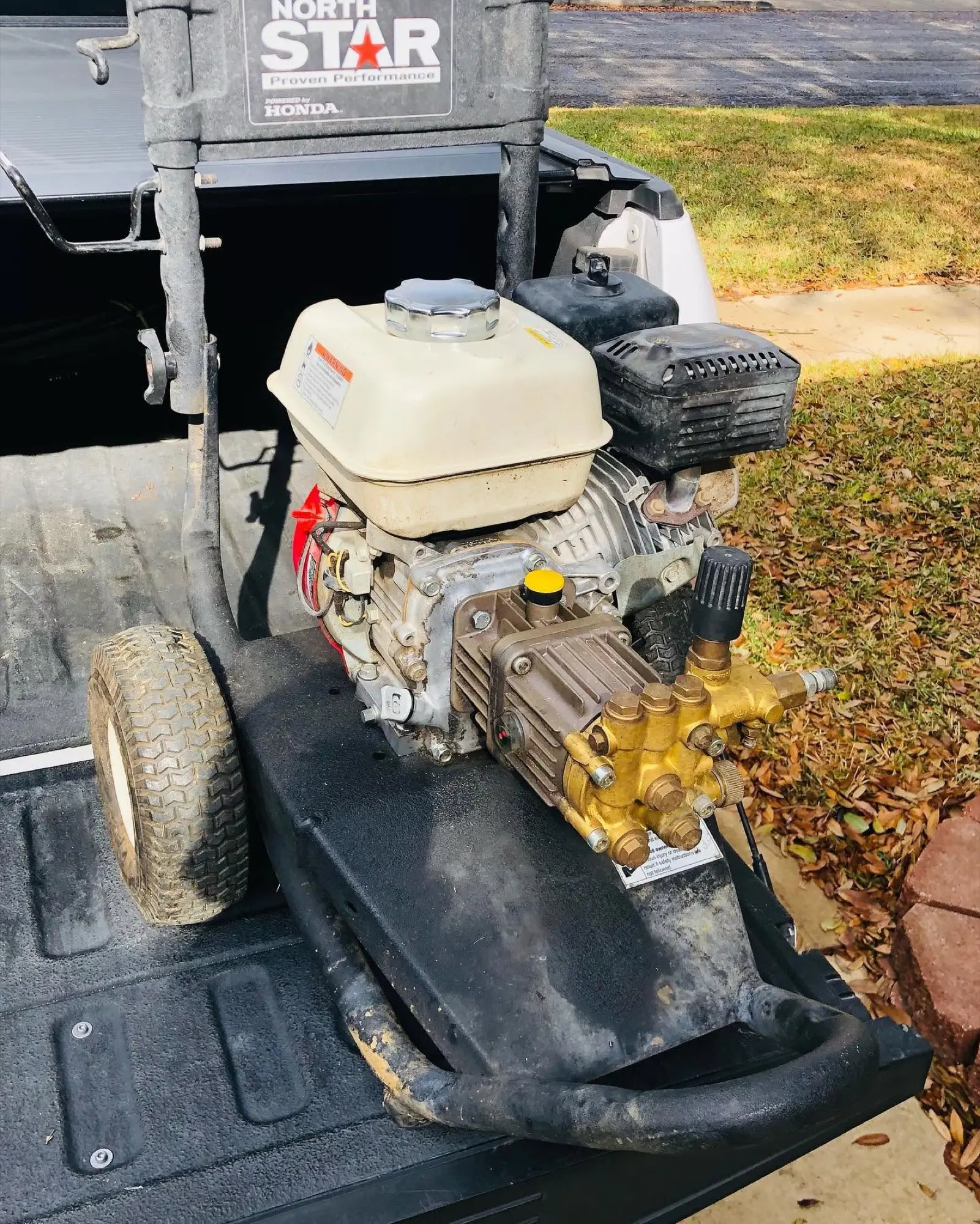 The first Live Oak pressure washer, a small gas unit, sitting in the open bed of a pickup truck beside a suburban lawn