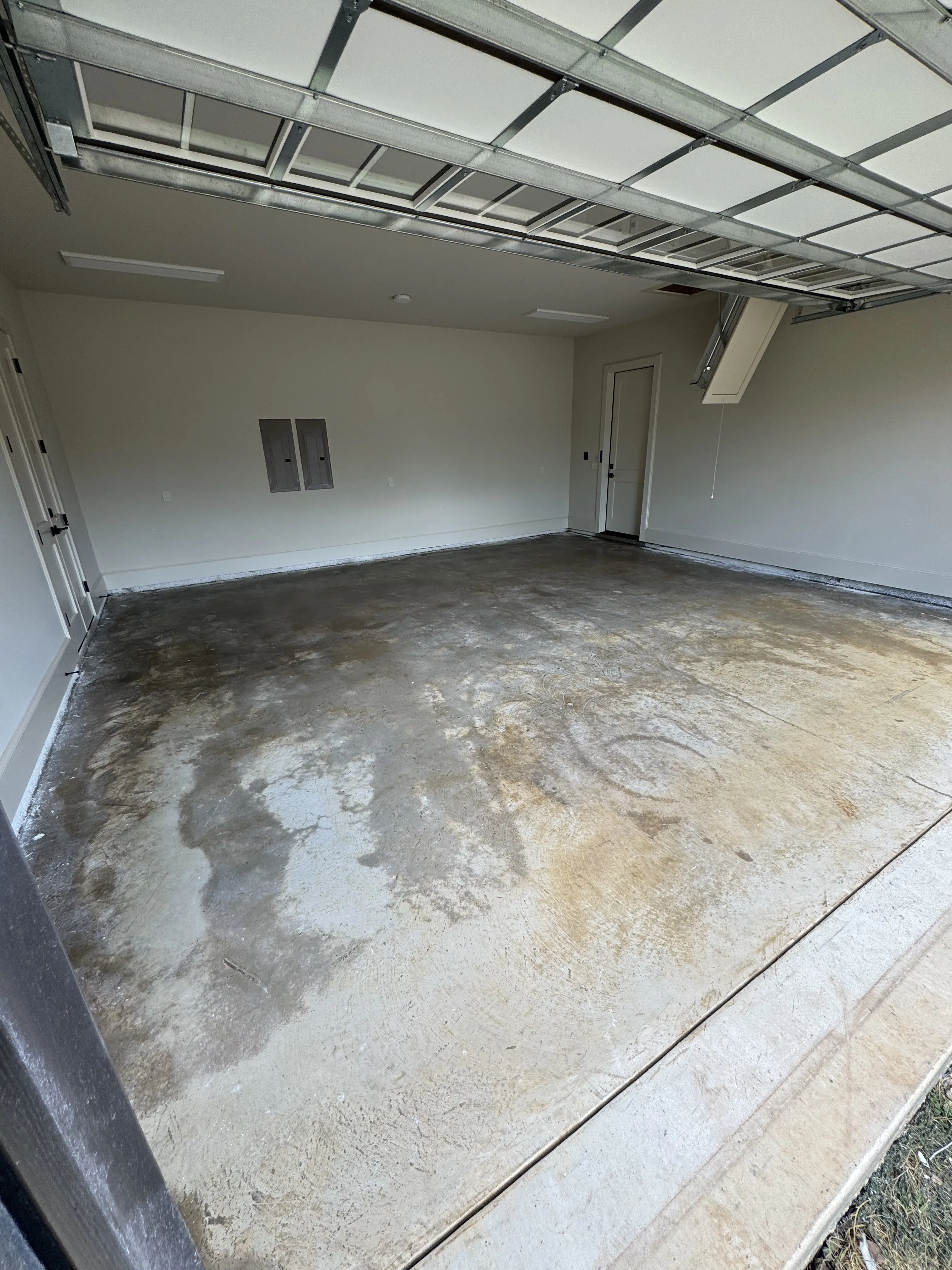 A finished garage bay with the floor dry and clean, the overhead door open to the driveway and the electrical panel on the side wall
