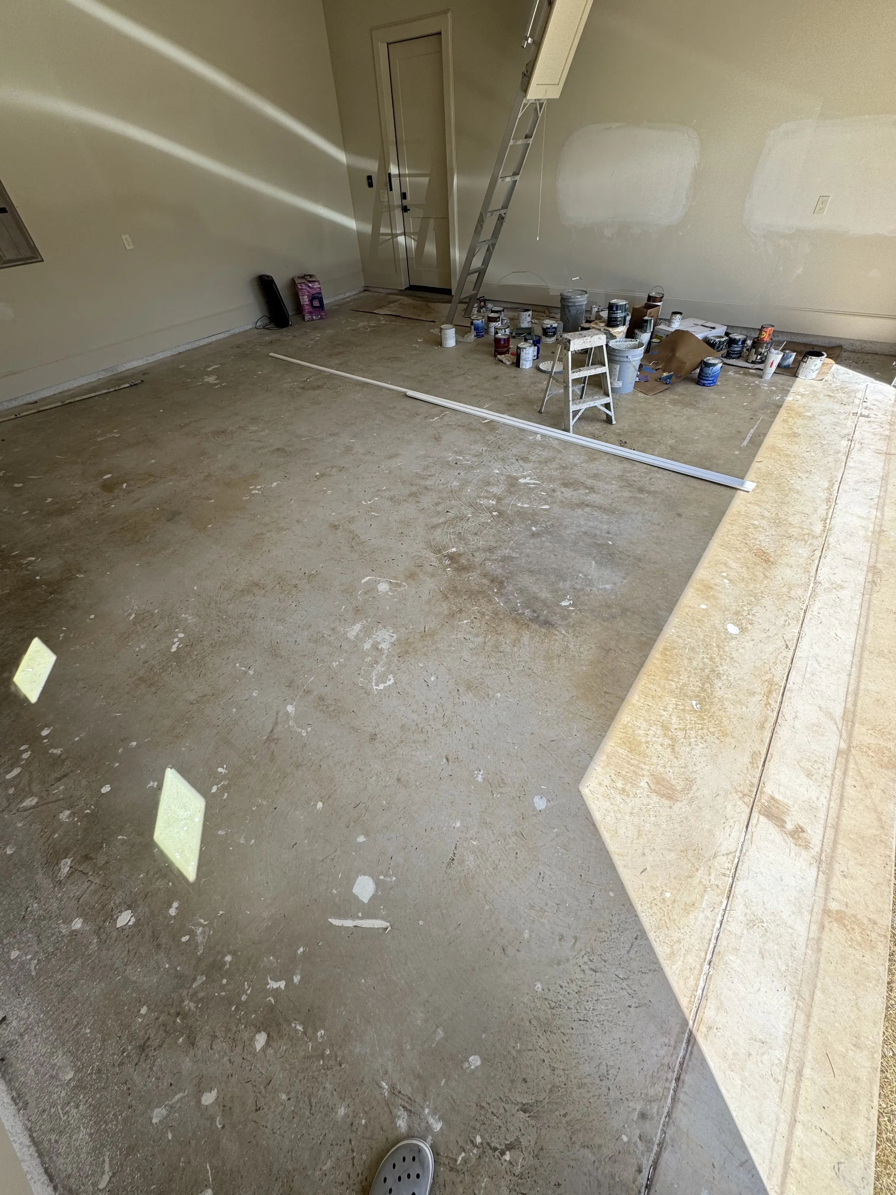 The garage mid-build in use as a paint station, cans and a stepladder along the back wall and drywall mud splattered across the bare slab