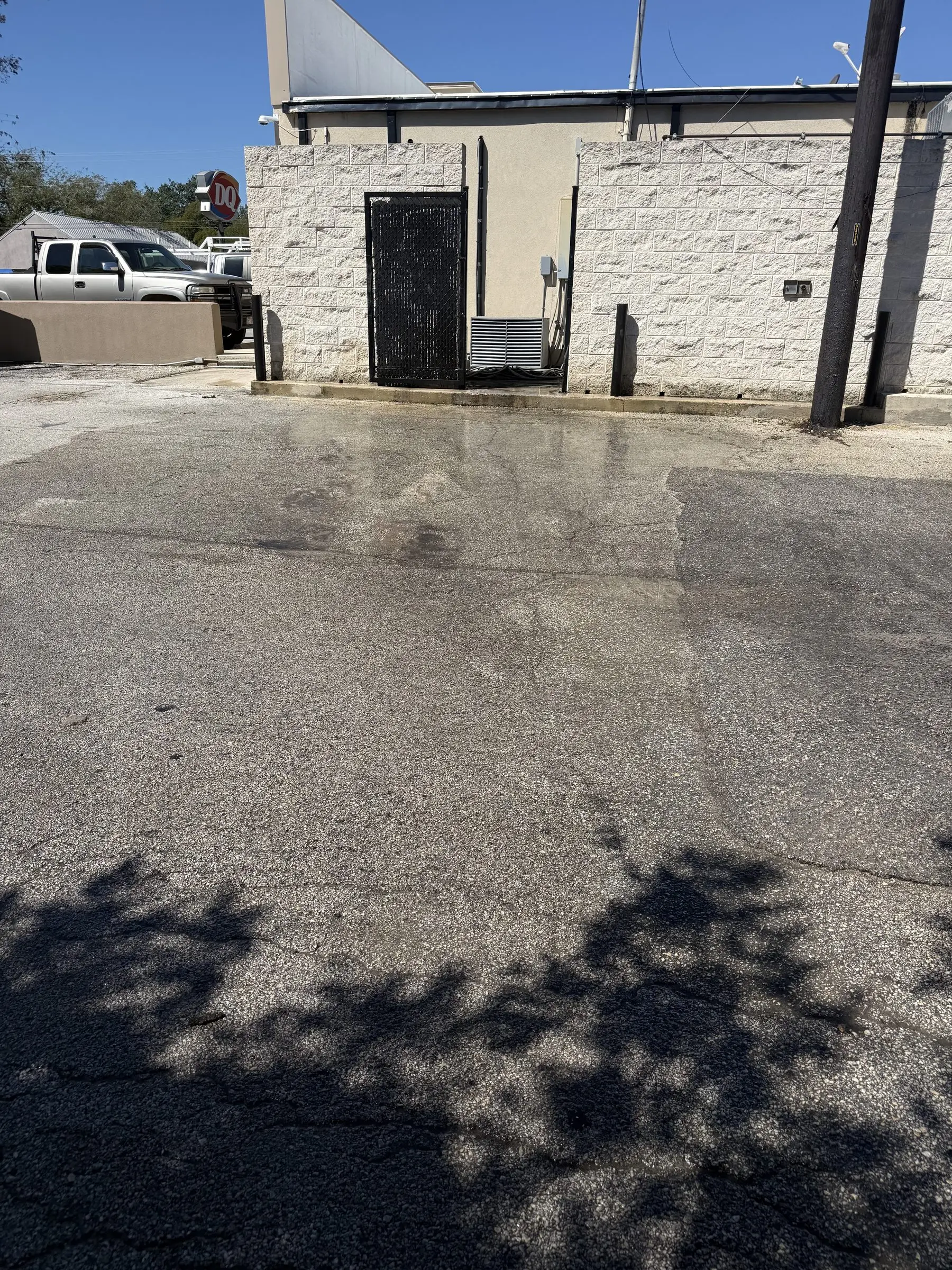 The cleaned asphalt behind the Blanco Dairy Queen, still damp, with the grease trap enclosure and the building's white stone wall behind it