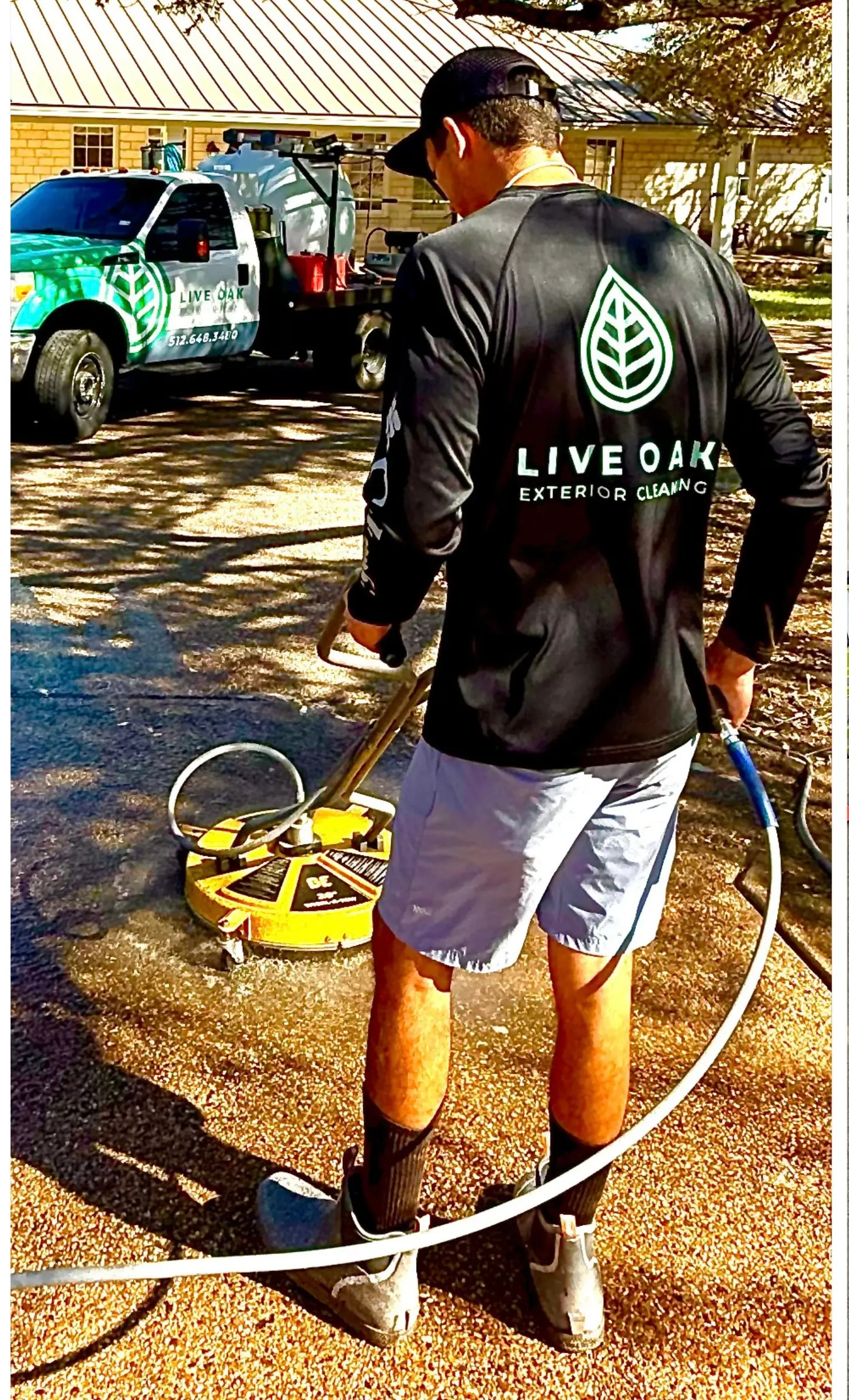 Jared Barker, owner of Live Oak Exterior Cleaning, using a surface cleaner on a driveway in Dripping Springs, TX