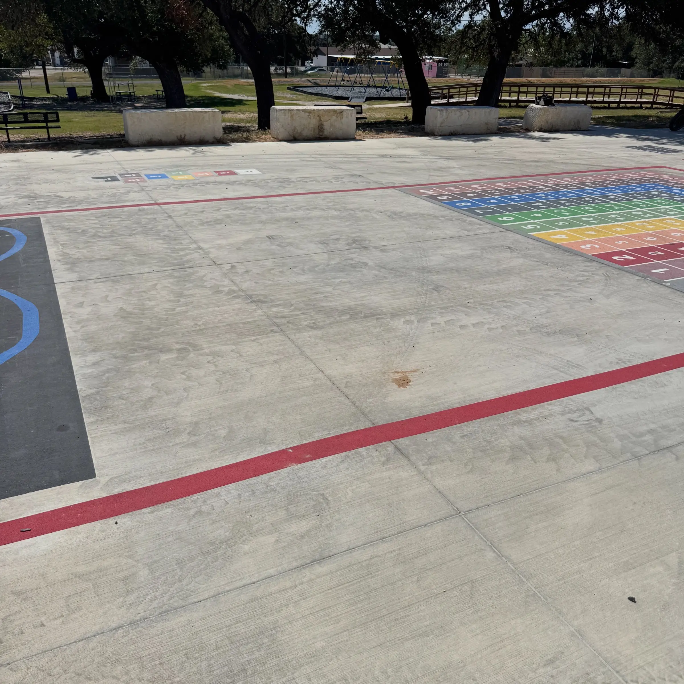 The wider Blanco ISD learning play surface before cleaning, its hopscotch grid and number chart ringed by a red border on dull mottled concrete