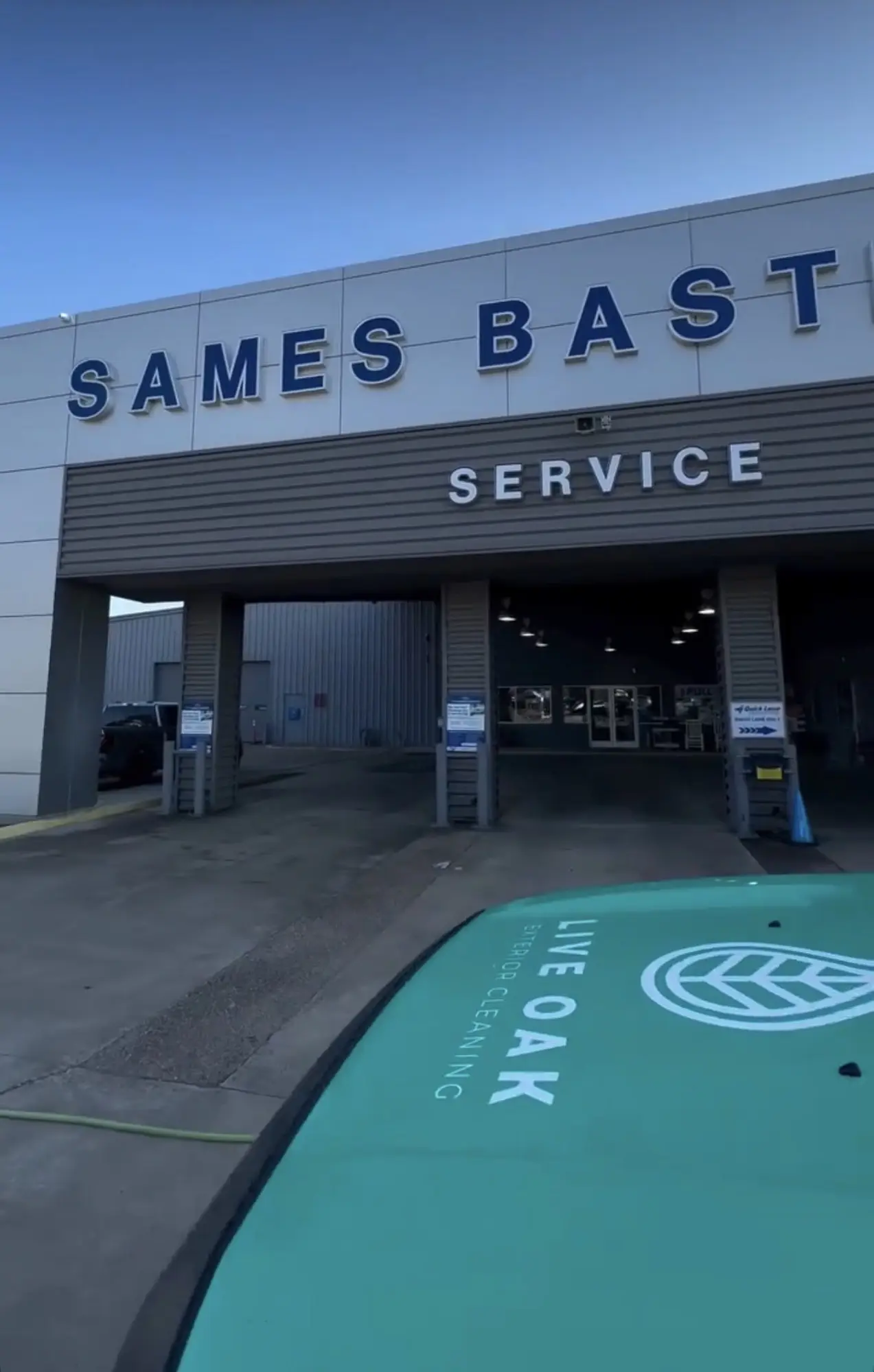 The service entrance of the Sames Bastrop dealership at dusk, open bay doors lit from inside, with the hood of the Live Oak truck in the foreground