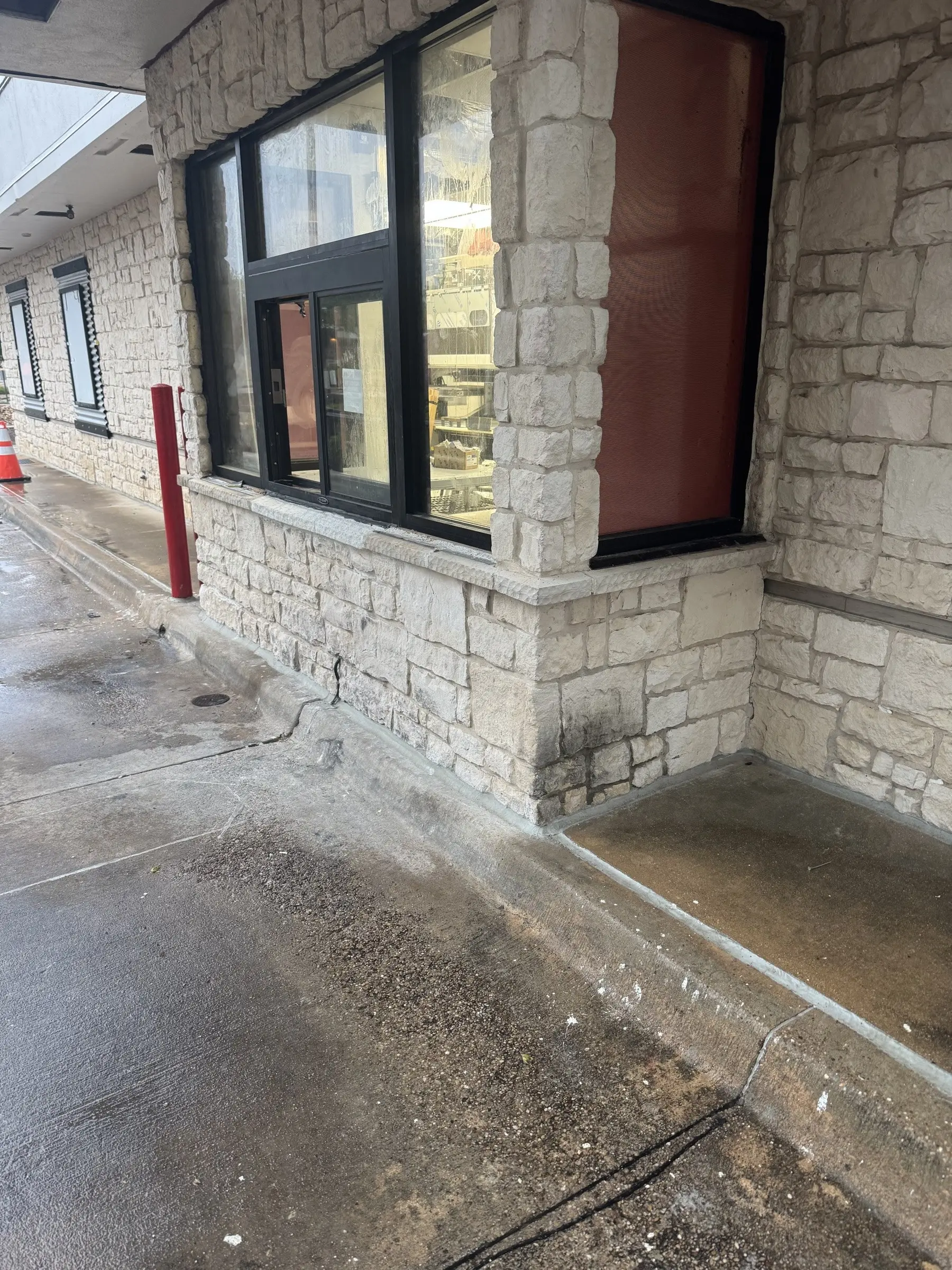 The corner of a white limestone restaurant building before cleaning, dark organic growth along the base of the stone and staining across the concrete apron