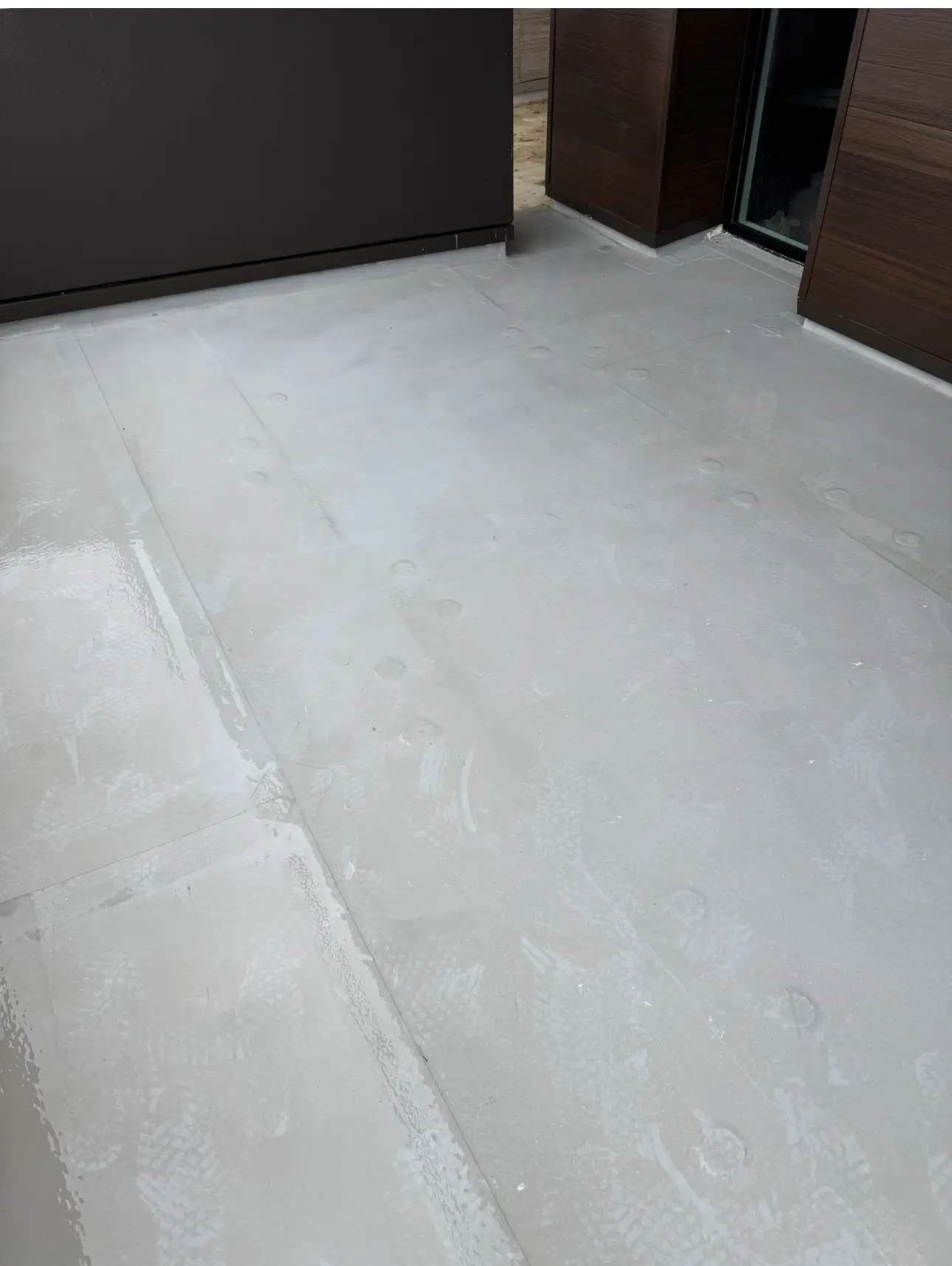 The same white TPO roof deck after cleaning, the membrane wet and uniformly white with the welded seams and fastener plates visible and no green growth left along the wall