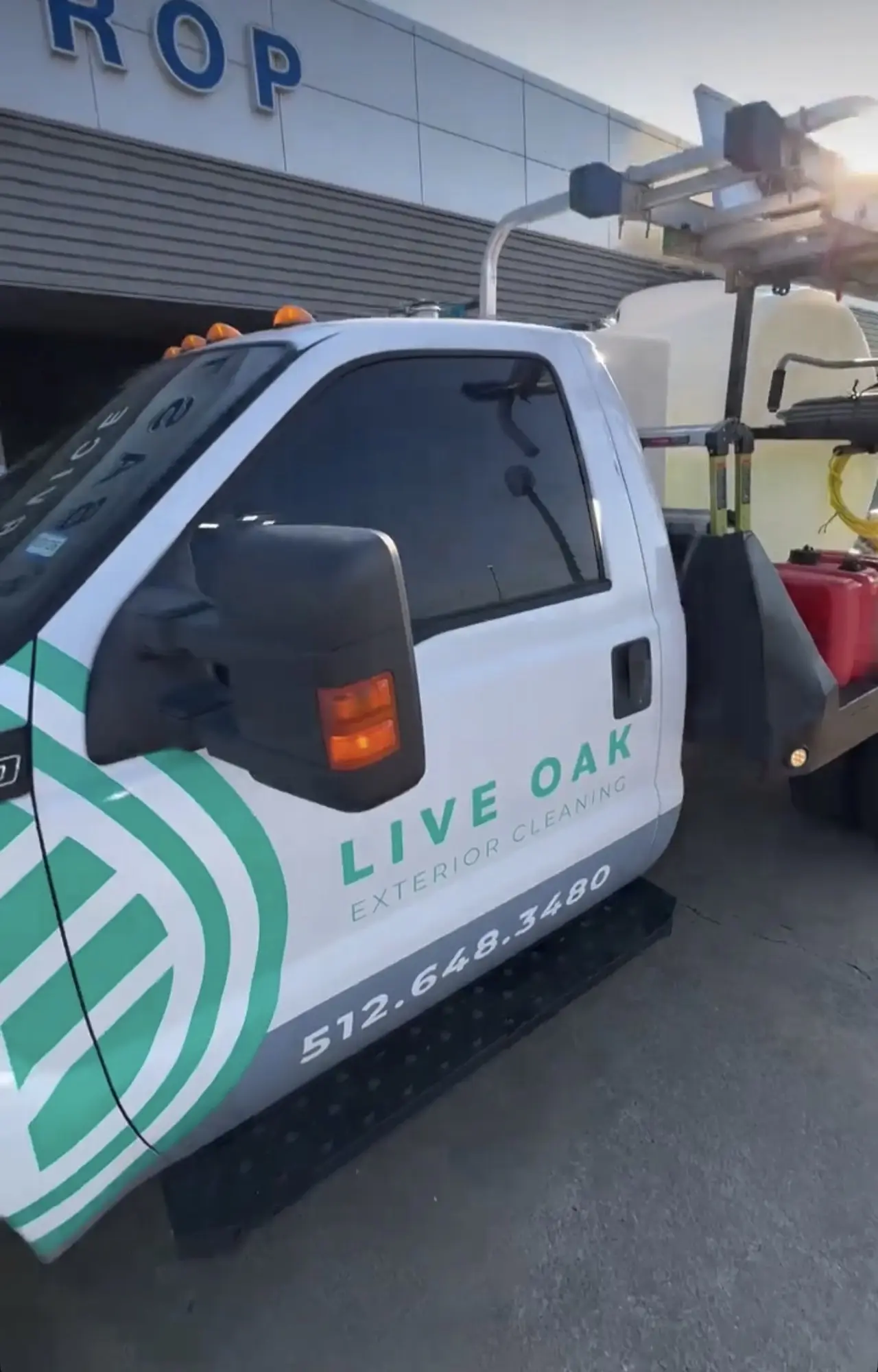 The Live Oak flatbed truck parked under the dealership service canopy with its tank and hose reels, amber beacons on the cab, late in the day